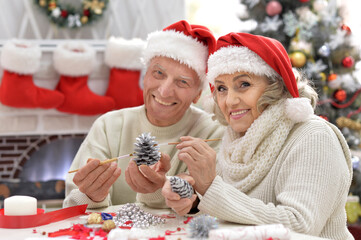 Canvas Print - Happy senior couple in Santa hats preparing for Christmas or New Year looking at the camera