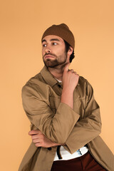 Wall Mural - young man in trendy jacket and beanie looking away isolated on beige