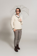 Wall Mural - full length view of stylish man standing under umbrella with hand in pocket on grey