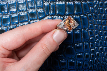 Sticker - Male's hand holding a ring with a brown stone on an artificial reptile skin background