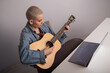 © Михаил Решетников - Young caucasian woman with short blonde hair playing guitar and watching training video on laptop.