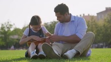 Happy Father And Daughter Playing Ukulele Sitting On Lawn In Park