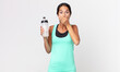 © kues1 - young hispanic woman covering mouth with hands with a shocked and holding a water bottle. fitness concept