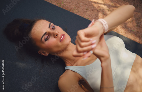 Top close up view young woman in sporty top lying on mat timing start finish work out sportive training outdoor looks at wristwatch. Healthy lifestyle, sport training activity use modern tech concept
