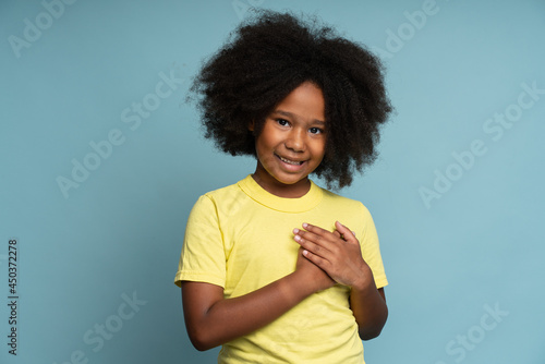 I promise to be honest. Portrait of happy responsible little girl holding her hand at her heart. Child swearing to tell truth. Studio shot isolated on blue background