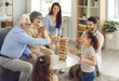 © Studio Romantic - Happy big family with little children enjoying the weekend at home, playing board games and having a good time together. Excited grandkids having fun watching grandpa take a wood block from the tower