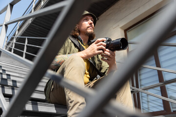 Portrait of young man, photographer, cameraman with professional camera, equipment during working summer day outdoors. Concept of occupation, job, education