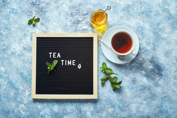 Wall Mural - Tea time. Black letter board with text on blue table with glass cup of tea with mint leaves