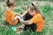 © Ольга Рязанцева - Two girls in identical T-shirts are sitting on the grass and playing 'Pop it'. Antistress. On open air.