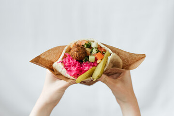 Wall Mural - shot of hands holding a vegetarian falafel with vegetables, and pickles wrapped in pita bread