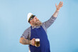 © Yaroslav Astakhov - Positive middle aged bearded man with overweight in sailor costume with apron holds mug of beer raising up hand on light blue background in studio
