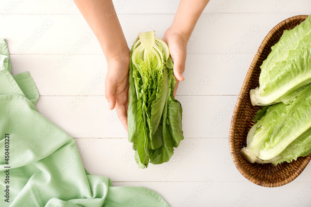 Female hands with fresh romaine lettuce on light wooden background