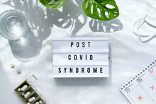 Text Post Covid Syndrome On Light Box In Hand. Long Covid Tail Awareness Design. Off White Background With Trendy Monstera Leaves And Long Shadows. Flat Lay, Top View Overhead.