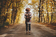 © sonyachny - Stylish woman traveller in hat with backpack walking on road in sunny autumn woods. Young female hipster hiking in fall forest, beautiful moment. Travel and wanderlust concept. Back view