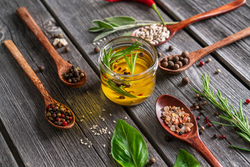 Homemade oil with spices on wooden background. Spoons with spices.