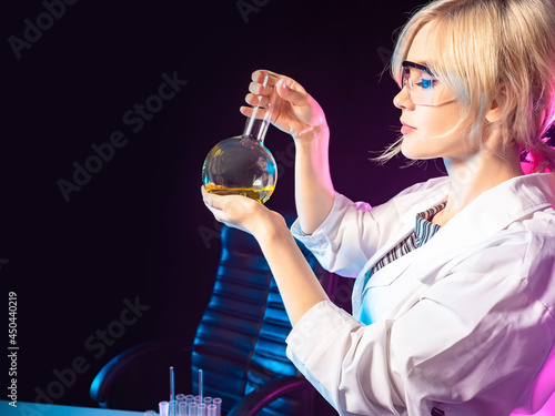 Chemist with a flask in her hands. Study of chemistry. A chemistry teacher demonstrates an experiment. Practical classes in chemistry. The girl is holding a flask with a yellow chemical liquid.