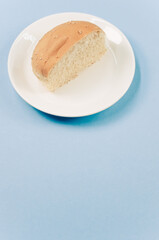 Sticker - Vertical shot of half bread bun on a plate isolated on blue background