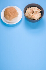 Sticker - Vertical shot of square crackers and bread bun isolated on blue background