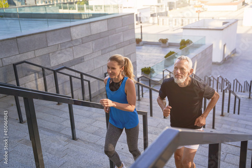 Mature couple in sportswear running up a flight of stairs in city while exercising together outdoors. Active sport, fitness, healthy lifestyle of middle aged people