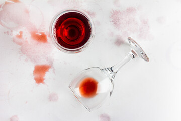 glass of red wine and overturned glass with leftover wine on a white background, drenched and stained with wine, top view