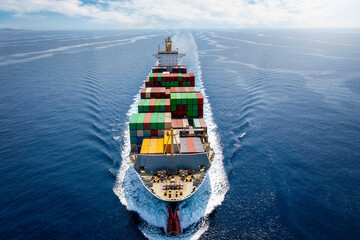 Aerial front view of a loaded container cargo ship in full motion on open sea