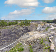Under A Blue Sky Is A View Of A Deep Rock Quarry Where Granite Rocks That Have Been Compressed Over Millions Of Years Are Excavated From Giant Boulders And Used Primarily Industrial Purposes. 