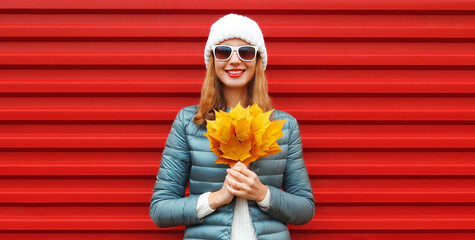 Canvas Print - Autumn portrait of happy smiling young woman holding an yellow maple leaves on a red background