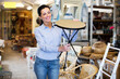 Smiling woman customer standing with wooden stool in shop for decor