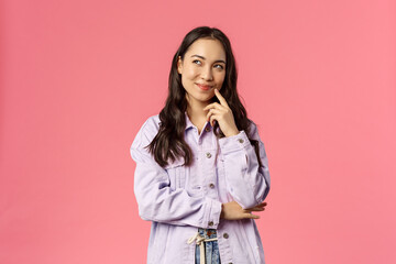 Hmm interesting. Portrait of smiling creative girl in denim jacket, thinking, have intriguing idea, smirk and look upper left corner, daydreaming, planning something for party, pink background