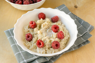 Wall Mural - Milk barley porridge with butter and raspberries in white bowl on wooden background