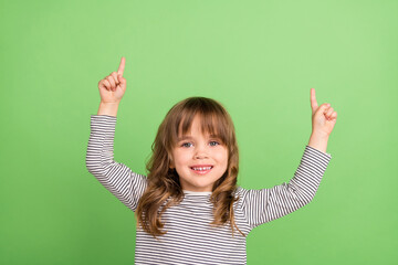 Wall Mural - Photo of cute little blond hair girl point up wear striped shirt isolated on green color backgound