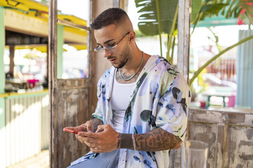 Canvas Print - Side view of a Spanish bearded attractive young male in stylish clothes typing on his phone