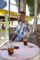 Wall Mural - Side view of a Spanish bearded attractive young male in stylish clothes posing sitting in a cafe