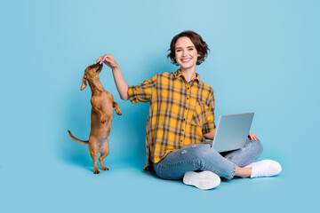 Poster - Photo of adorable lady sit floor hold pc play funny dog wear plaid shirt jeans shoes isolated blue color background