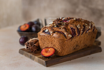 Wall Mural - Homemade spicy plum cake decorated with almond on a wooden serving board, concrete background. Loaf cake with plum, spices and almond.