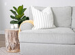 A modern farmhouse home decor scene with couch, wood stump end table, throw pillows and fiddle leaf fig houseplant.