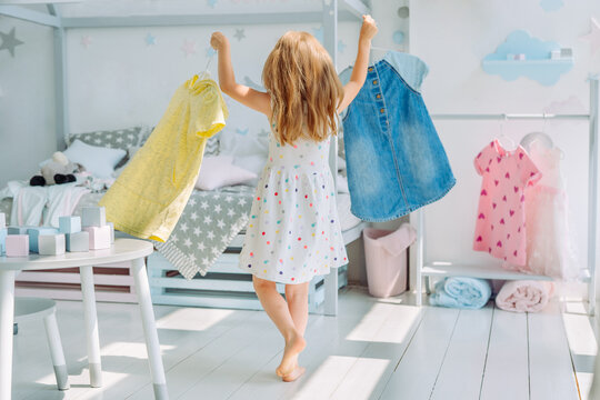 Beautiful little girl choosing a dress in the kids room