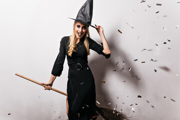Wall Mural - Refined fair-haired woman posing in witch costume. Studio portrait of pretty caucasian girl having fun at halloween party.