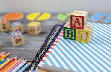 Wall Mural - Wooden alphabet blocks on wooden background. Back to school, games for kindergarten, preschool education. Abacus, pencils, notebooks, blocks on the table.