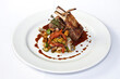 Roasted rack of lamb or rack of veal accompanied with vegetables and sauce, served on white plate over white background