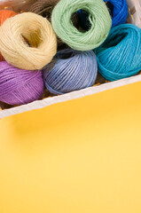 Canvas Print - Vertical shot of colorful yarns on a box isolated on yellow background