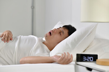 Young Asian man sleeping and snoring loudly lying in the bed.