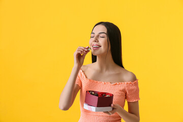 Wall Mural - Beautiful young woman with box of chocolate candies on color background