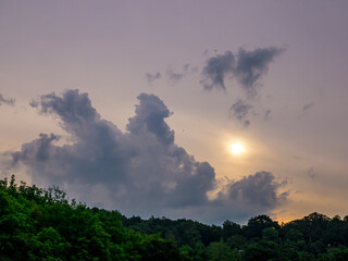 Wall Mural - Massive cloud over the hill and the sun obscured by a layer of clouds early in the morning