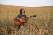 © Ilya - A girl in glasses with an old acoustic guitar stands with her eyes closed in a wheat field lit by the rays of the setting sun