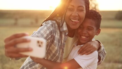 Wall Mural - A cheerful afro-american mother is taking selfie photo with her son during picnic time outside