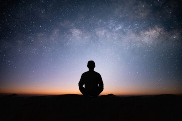 Wall Mural - Silhouette of young traveler sitting and meditating with the star and milky way alone on top of the mountain. He enjoyed traveling and was successful when he reached the summit.
