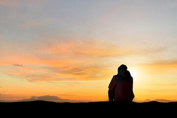 Wall Mural - Silhouette of young man sitting and watching beautiful view overcast sky, sunset alone on top of the mountain. He enjoyed traveling and was successful when he reached the summit.