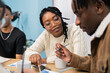 © ABCreative - A beautiful young woman with a darker complexion and black braids sits in her office wearing glasses looking at her co-worker with interest, with a gentle smile I try to get his attention