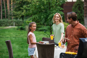 Wall Mural - Smiling woman and girl looking at father grilling food outdoors